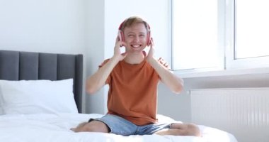 Evde kulaklıkla müzik dinleyen ve yatakta dans eden mutlu bir adam.