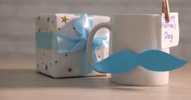 Mutlu Babalar Günü kartı, kağıt bıyık ve tahta masanın üzerinde tuğla duvara yapıştırılmış hediye kutusu, yakın plan. Kamera sağa hareket ediyor