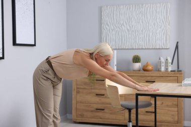 Olgun bir kadın ofiste masaya yaslanıyor.