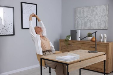 Gri duvarın yanındaki masada uzanan olgun bir kadın.