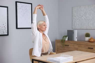 Gri duvarın yanındaki masada uzanan olgun bir kadın.