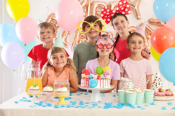 Doğum günü kutlaması. Masadaki çocuklar lezzetli pastalar ve dekoratif odalarda farklı şeyler yiyorlar.