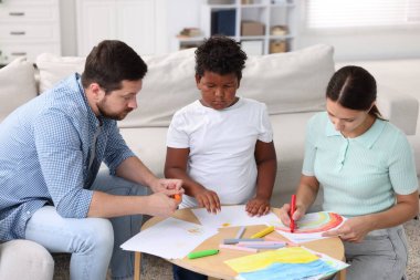 Evlat edinme. Ebeveynler ve oğulları kapalı bir masada birlikte resim çiziyorlar.