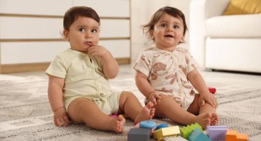 Evde yerde oyuncaklarla oynayan şirin ikiz bebekler.