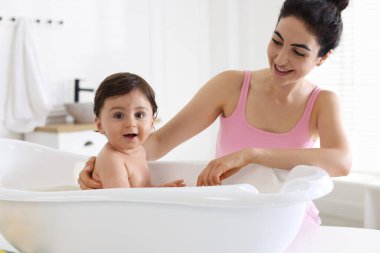 Anne küçük bebeğini evde yıkıyor.
