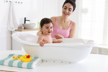 Anne küçük bebeğini evde yıkıyor.