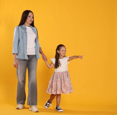 Kızı, annesine sarı arka planda bir şey gösteriyor.