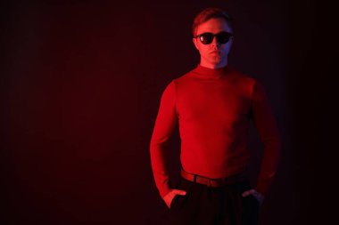 Güneş gözlüğü takan yakışıklı bir adam karanlık arka plana karşı neon ışıklar takıyor. Metin için boşluk