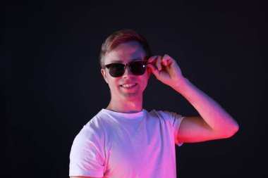 Siyah arka planda, neon ışıklarda güneş gözlüğü takan gülümseyen adam