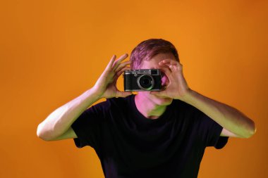 Kameralı bir adam turuncu arka planda neon ışıklarla fotoğraf çekiyor.