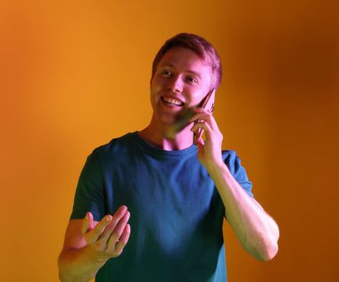 Akıllı telefonda konuşan mutlu bir adam neon ışıklarıyla turuncu arka planda
