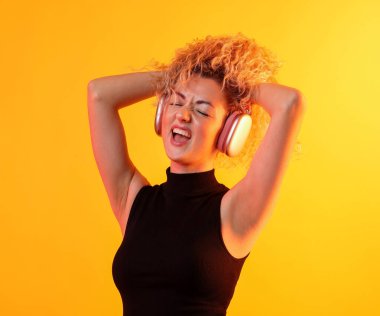 Mutlu kadın kulaklıkla müzik dinliyor ve sarı arka planda dans ediyor.