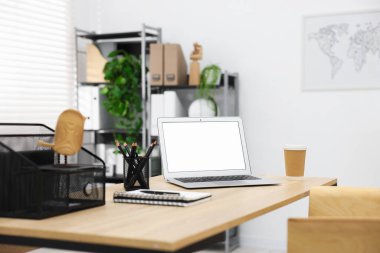 Ofisteki ahşap masada dizüstü bilgisayarı, kahvesi ve kırtasiyesi olan şık bir iş yeri.