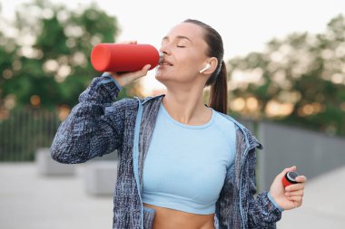 Kulaklıklı genç bir kadın dışarı çıkmadan önce su içiyor.