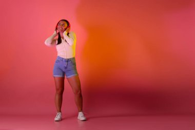 Kulaklıklı gülümseyen kadın pembe arka planda neon ışıklarla müzik dinliyor. Metin için boşluk