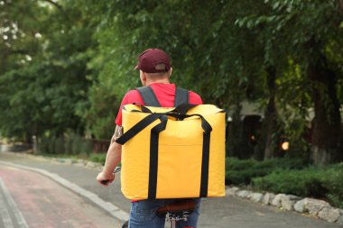Termo çantalı bir kurye dışarıda bisiklet sürüyor, arkadan bakıyor. Yemek dağıtım servisi.
