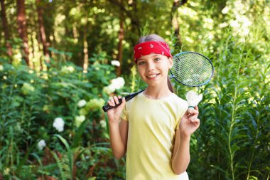 Bandana 'da badminton raketiyle gülümseyen küçük bir kızın portresi.