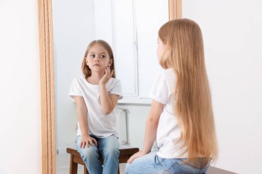Üzgün küçük kız aynada kendine bakıyor.