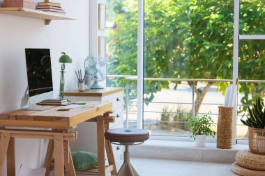 Ev çalışma alanı. Modern bilgisayar ve kırtasiye malzemeleri pencerenin yanındaki ahşap masada.