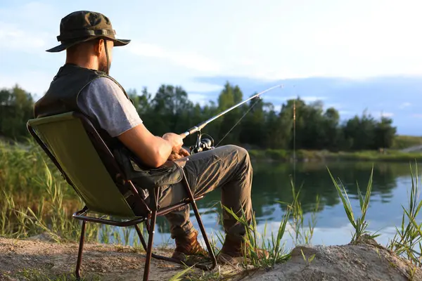 Yazın sandalyede oturan ve göl kenarında balık tutan oltalı balıkçı.