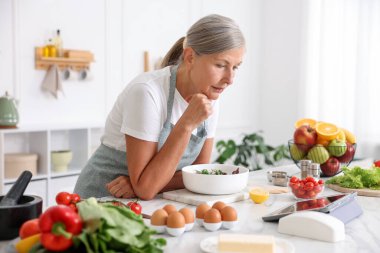 Üst düzey kadın mutfakta beyaz mermer masada salata pişirirken tablet kullanıyor.