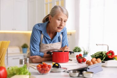 Mutfaktaki beyaz mermer masada yemek pişirirken tablet kullanan yaşlı kadın.