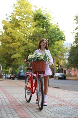 Bisikletin yanında güzel bir genç kız ve şehir caddesinde bir sepet çiçek.