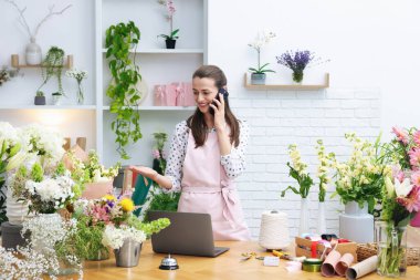 Profesyonel çiçekçi dükkanda çalışırken akıllı telefondan konuşuyor.
