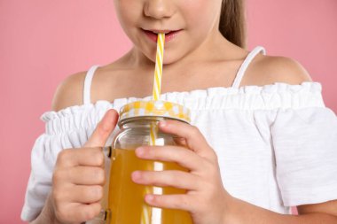 Küçük kız pembe arka planda samandan meyve suyu içiyor, yakın plan.