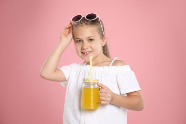 Meyve suyu ve pembe arka planda pipet içen küçük bir kız.