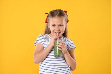 Küçük kız turuncu arka planda samandan meyve suyu içiyor.