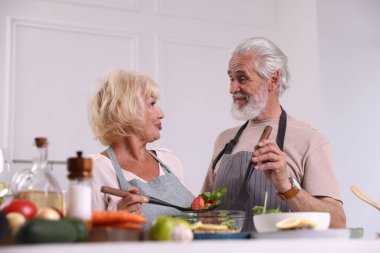 Yaşlı çift içeride birlikte yemek pişiriyor.