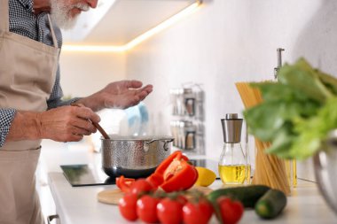 Mutfaktaki mutfağın tepesinde yemek pişiren yaşlı adam, yakın plan.