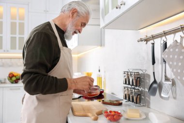 Mutfakta tezgahta yaşlı bir adam yemek pişiriyor.