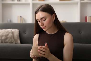 Evdeki kanepenin yanında bir bardak içkiyle güzel bir kadın.