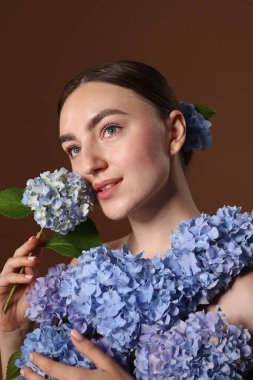 Kahverengi arka planda hortensiya çiçekleri olan güzel genç bir kadın.