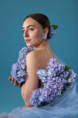 Mavi arka planda hortensiya çiçekleri olan güzel bir kadının portresi.