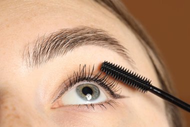 Kahverengi arka planda kirpiklerine rimel süren kadın, yakın plan.