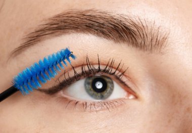 Bir kadın kirpiklerine rimel sürüyor, yakın plan.