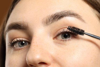 Kahverengi arka planda kirpiklerine rimel süren kadın, yakın plan.
