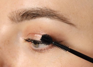 Bir kadın kirpiklerine rimel sürüyor, yakın plan.