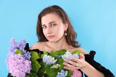 Açık mavi arka planda Hortensiya çiçekleri olan güzel bir kadının portresi.