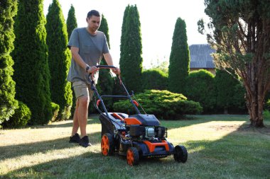 Bahçede çim biçme makinesiyle yeşil çim biçen bir adam