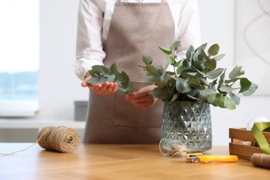 Çiçekçinin ahşap masasında okaliptüs dallarından güzel bir buket yapıyor.