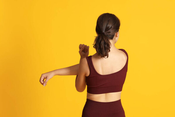 Teenage girl in sportswear stretching on orange background, back view