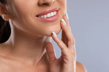 Açık gri arka planda güzel sağlıklı dişleri olan kadın, yakın plan.