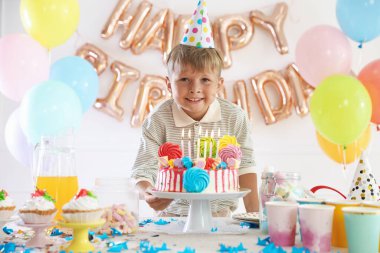 Doğum günü kutlaması. Masadaki tatlı küçük çocuk lezzetli pastayla ve çeşitli ziyafetlerle süslenmiş odada.