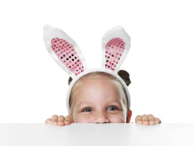 Tavşan kulaklı meraklı küçük kız beyaz arka planda masanın üstünden bakıyor.