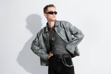 Beyaz arka planda şık ceket ve güneş gözlüğü takan yakışıklı bir genç.