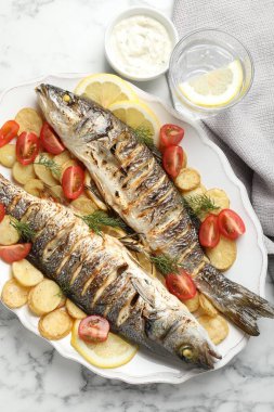 Beyaz mermer masada patates, domates, sos ve limonla servis edilen kızarmış deniz kabuğu balığı. Ev yapımı deniz ürünleri yemeği.